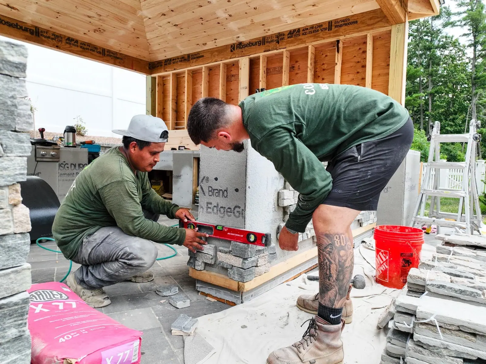 Contrast Landscape crew leveling the stone veneer of an outdoor kitchen island under a new pavilion