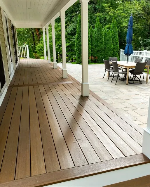 Covered porch with composite decking, white columns and a patio beyond
