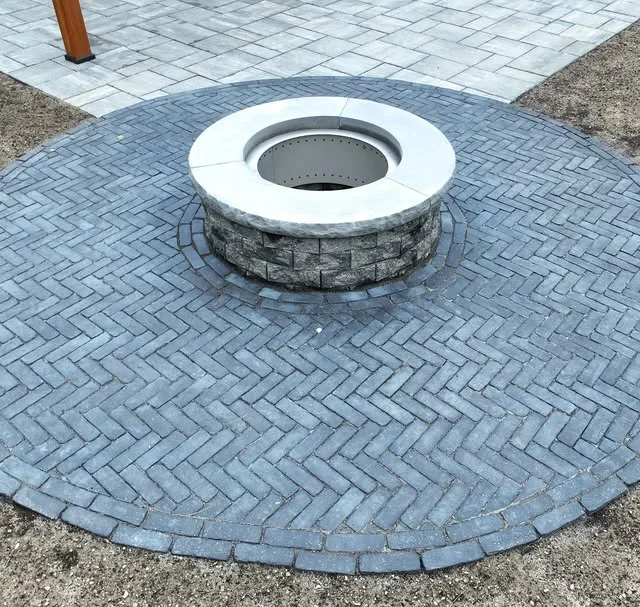 Round herringbone paver patio with a stone fire pit and Adirondack chairs