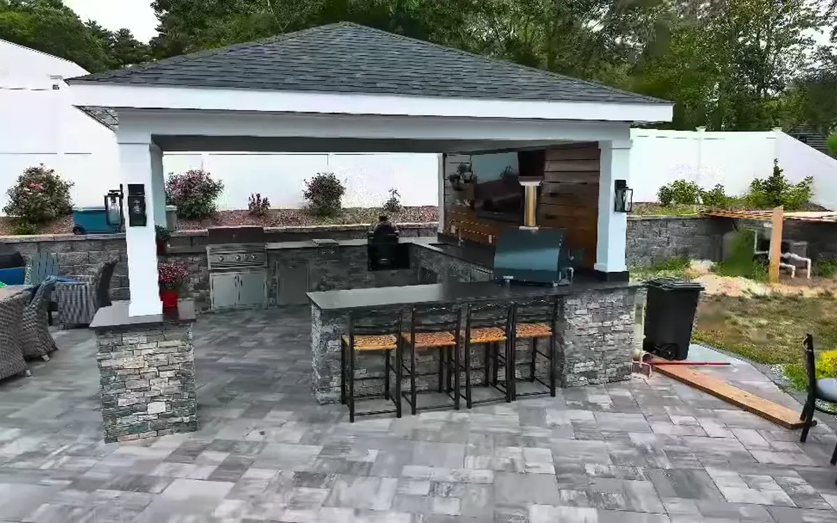 Outdoor kitchen with stone counters and a covered seating area